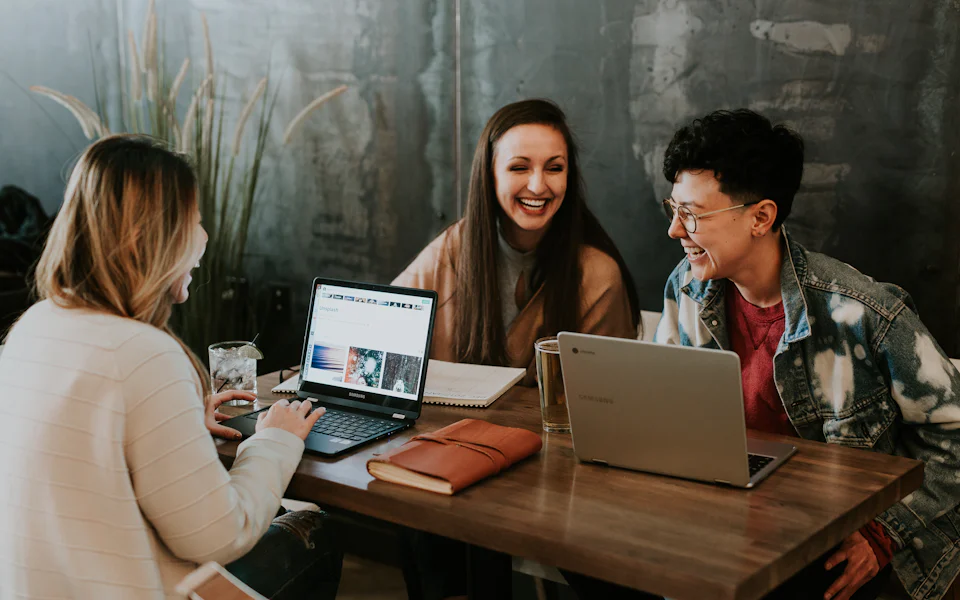 Three friends smiling while browsing games on a laptop in a cafe